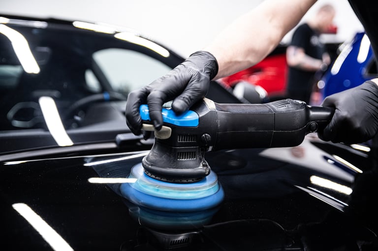 Mechanic wearing black gloves polishing car paint with a machine in a detailing studio. Close-up view of hands using a polisher on the vehicle's surface to achieve a glossy finish