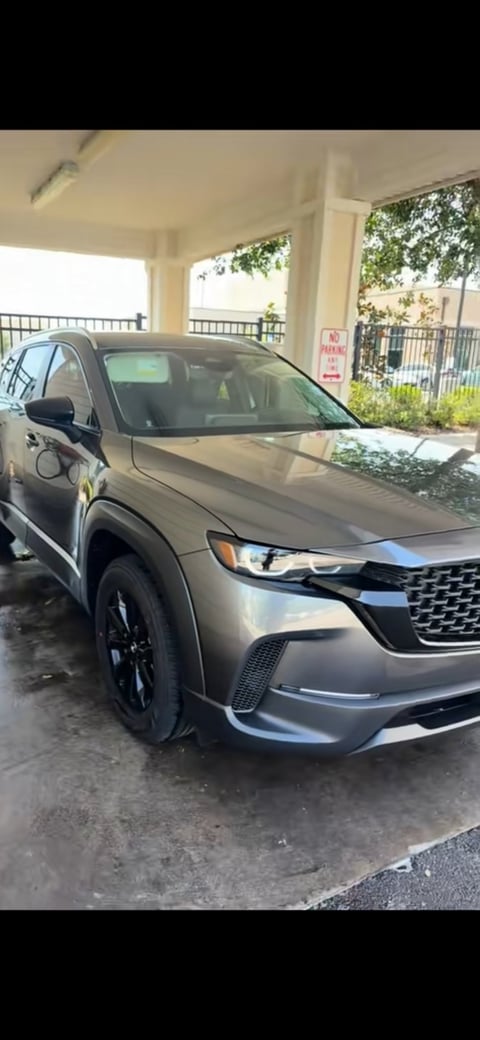 Silver Kia SUV parked in covered garage with metal railing and landscaping visible in background