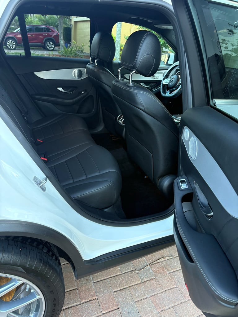 Interior of white car with open door showing black leather seats, steering wheel, and dashboard with parked vehicles visible outside