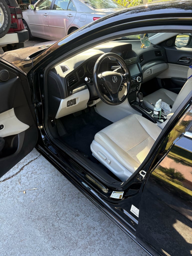 Black Acura sedan with drivers side door open, showing white and gray interior with steering wheel and dashboard visible, parked outdoors