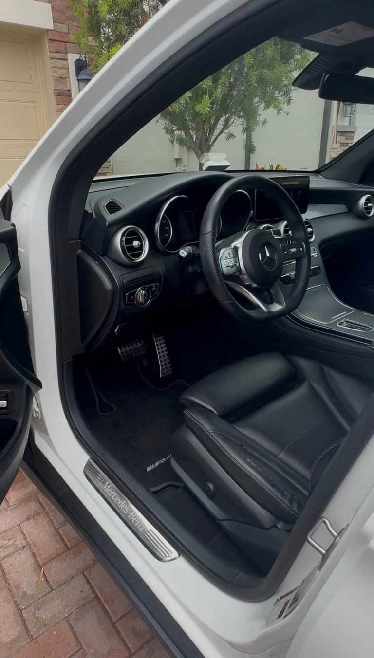 Interior of a white Mercedes-AMG sports car showing black leather seats, steering wheel, and dashboard with open door