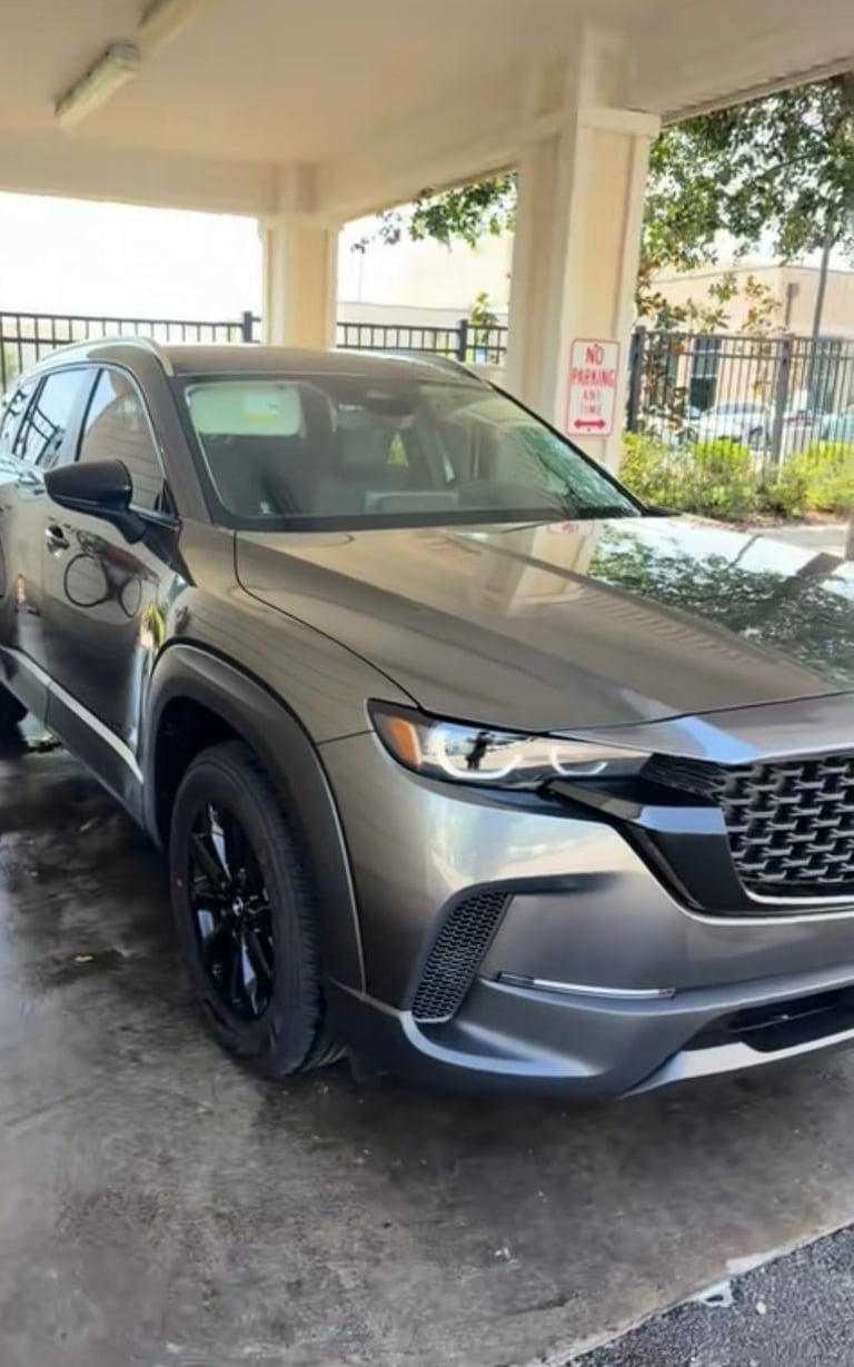 Silver Kia SUV parked in a covered lot with charging cable attached, outdoor parking area visible in background