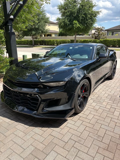 Black Chevrolet Camaro parked on brick paver driveway in suburban neighborhood