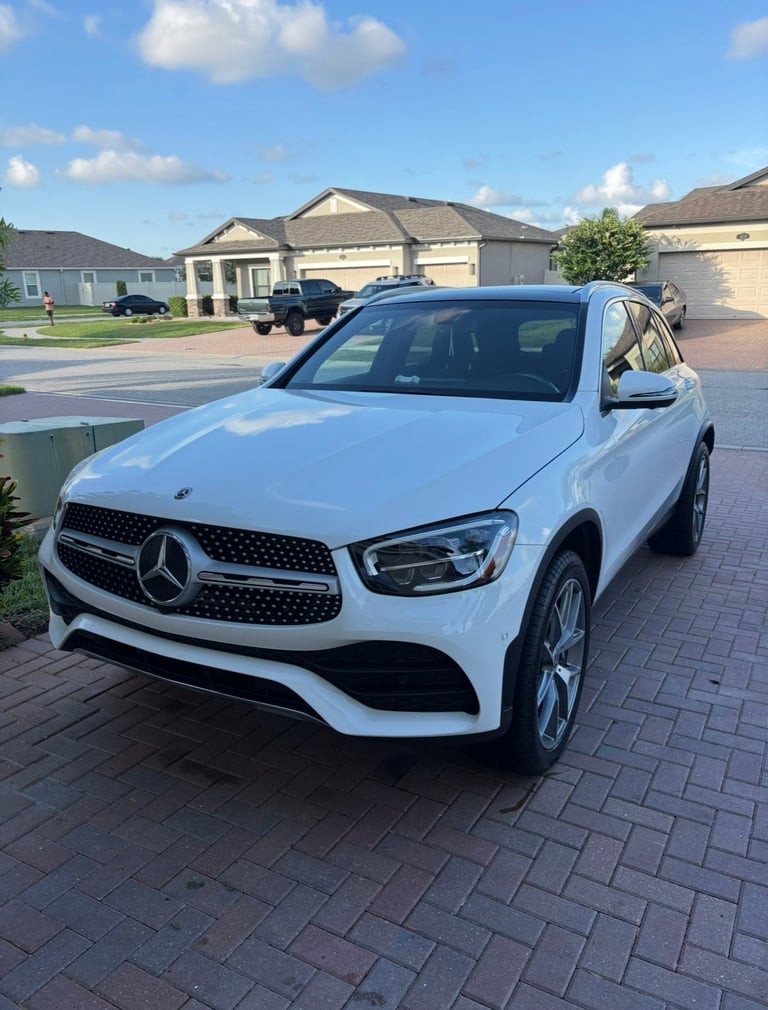 White Mercedes-Benz SUV parked on a brick driveway in front of residential homes on a sunny day