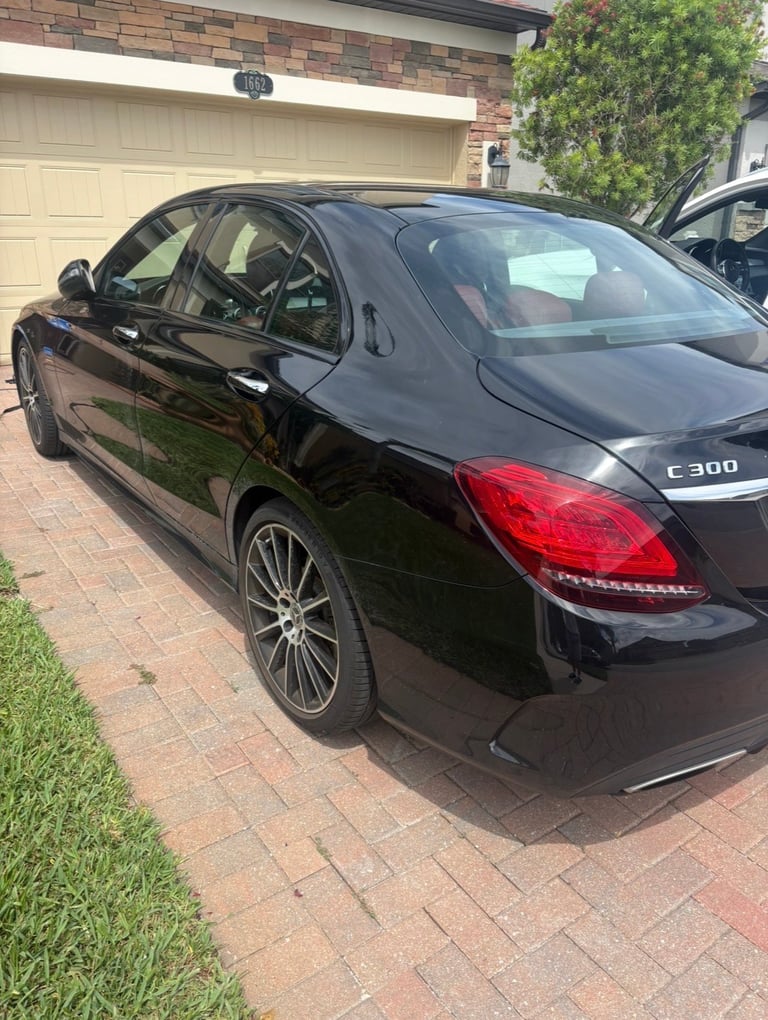 Black Mercedes C300 sedan parked in driveway with brick garage and green ivy in background