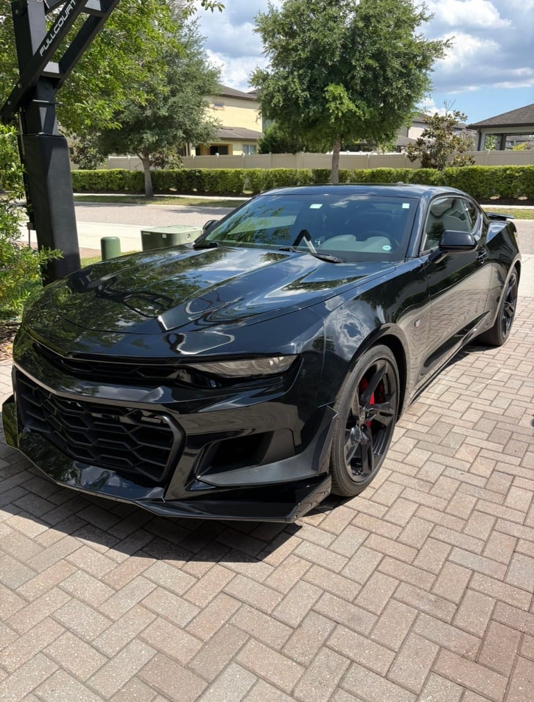 Black Chevrolet Camaro sports car parked on a residential driveway on a sunny day