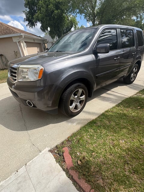 Dark gray Honda Element SUV parked in a driveway on a sunny day with trees and a house visible in the background