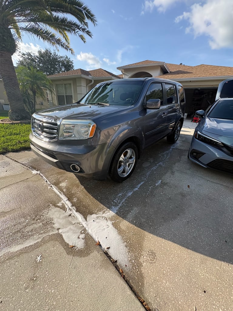 Gray Honda Pilot SUV parked in a driveway in front of a Florida home with palm trees