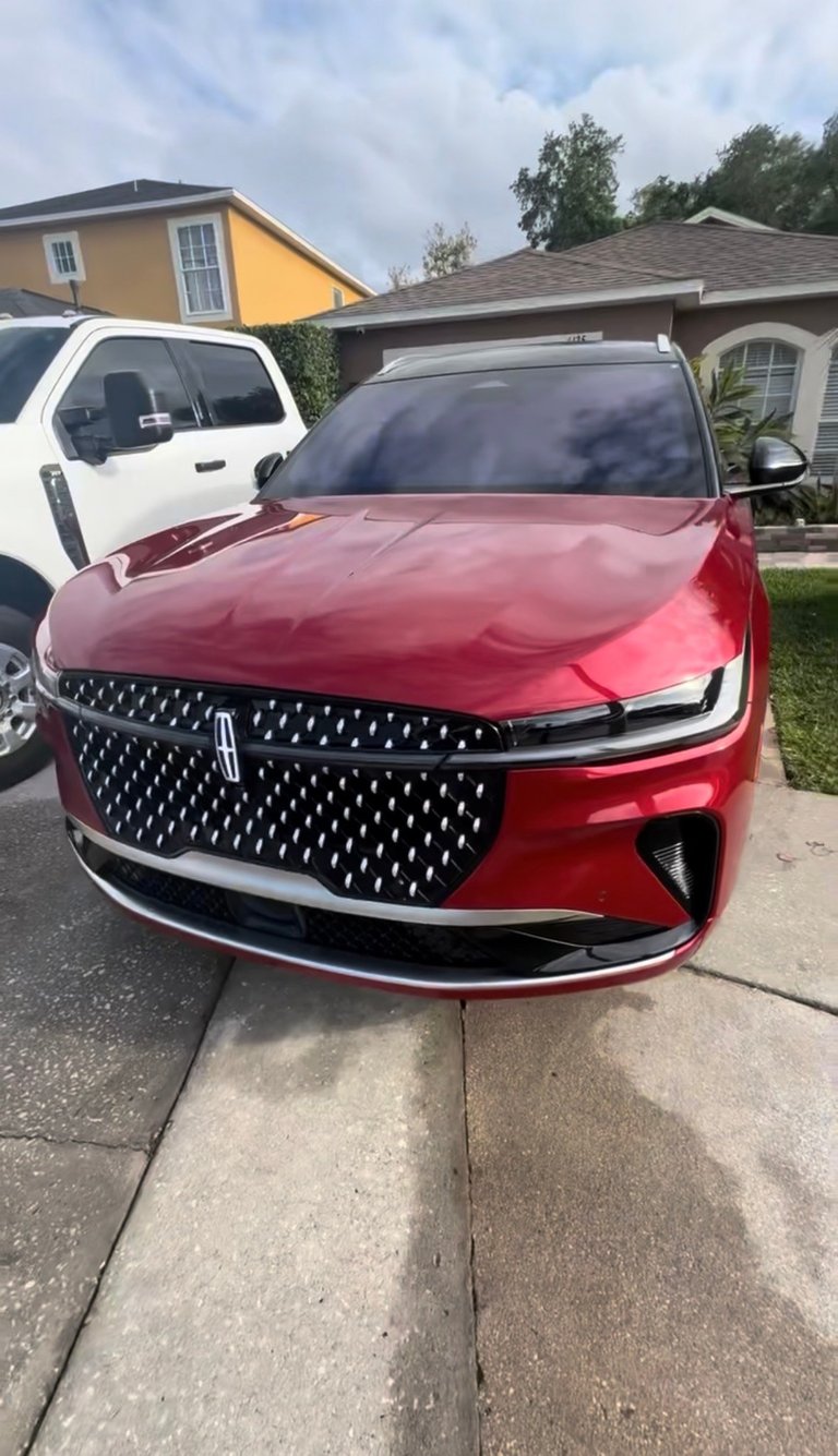 Red Lincoln sedan with distinctive grille parked in residential driveway with white SUV and houses visible in background