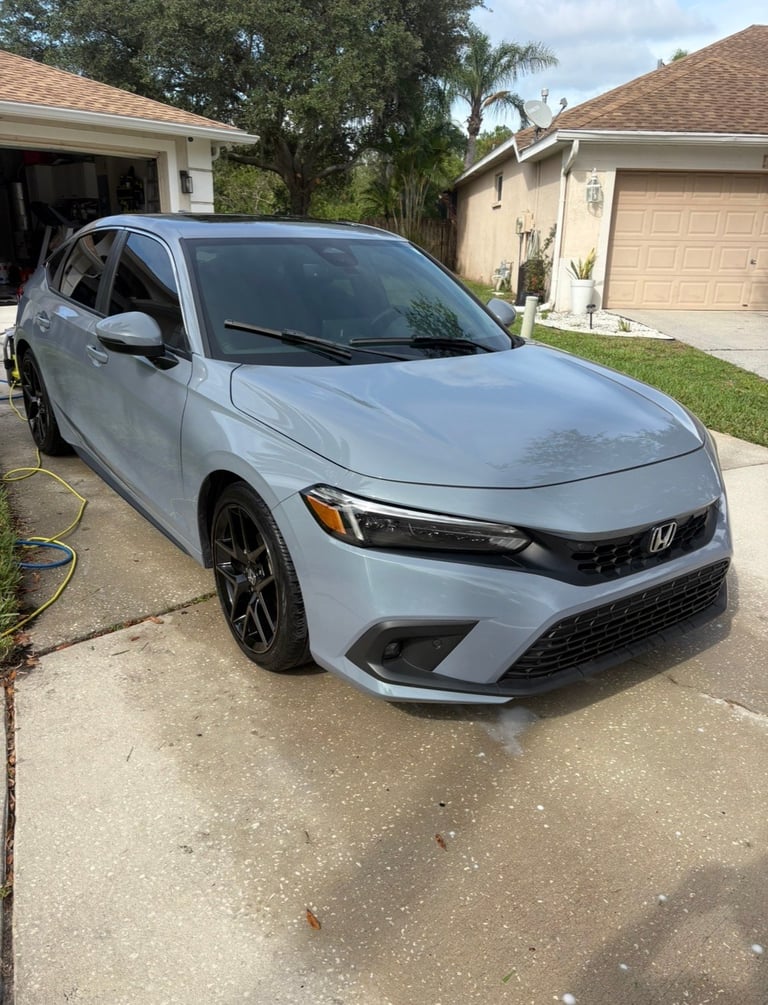 Light blue Honda hatchback parked in a residential driveway next to a charging cable